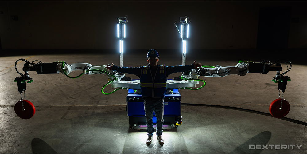 Dexterity’s Mech robot with arms outstretched, holding two weights, with a human standing in front. Image source: dexterity.ai